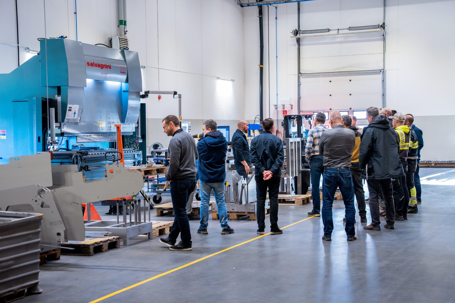 En grupp människor besöker en fabrik på Hydria Water, omgiven av maskiner och industriell utrustning.